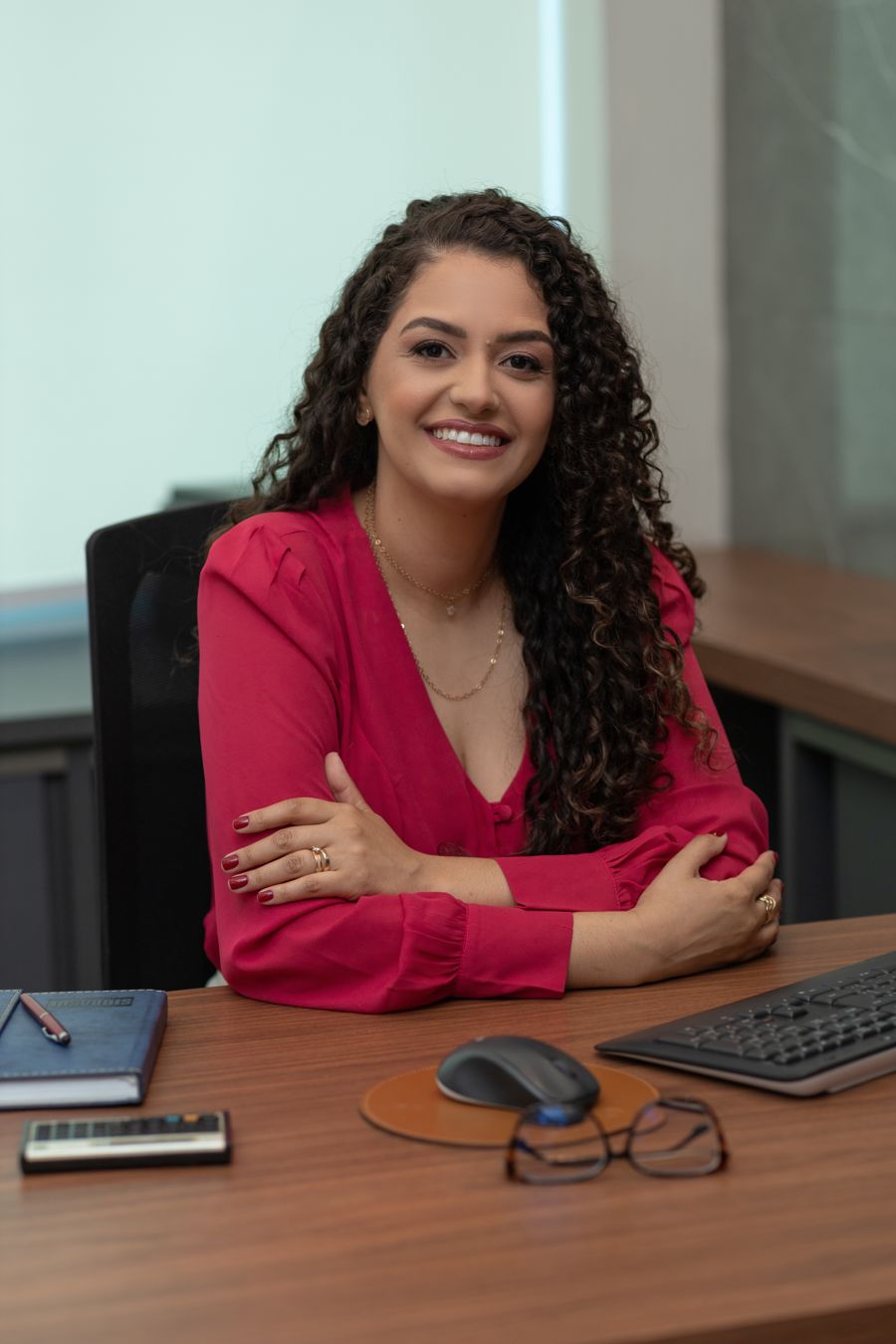 Adriana Paiva sorrindo à mesa de trabalho, de blusa rosa